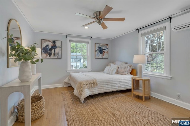 bedroom featuring light wood finished floors, multiple windows, baseboards, and a wall unit AC