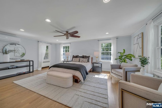 bedroom with radiator, wood finished floors, recessed lighting, a wall mounted AC, and baseboards