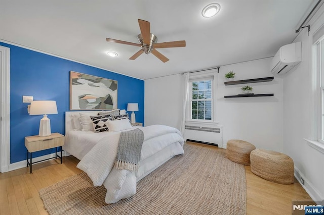 bedroom featuring a wall unit AC, baseboards, radiator, ceiling fan, and wood finished floors