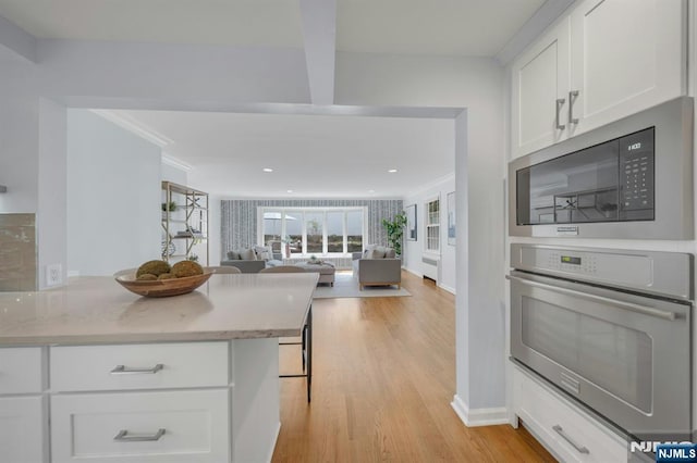 kitchen featuring stainless steel oven, light wood finished floors, black microwave, open floor plan, and white cabinets