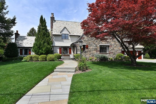 tudor house featuring stone siding, a high end roof, a chimney, and a front yard