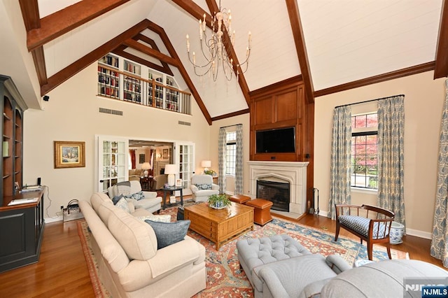 living room with baseboards, a fireplace with flush hearth, wood finished floors, beamed ceiling, and visible vents