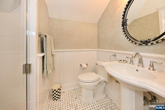 bathroom with toilet, a sink, wainscoting, and a shower stall