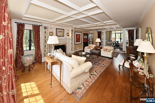 living area featuring coffered ceiling, ornamental molding, wood finished floors, and a fireplace
