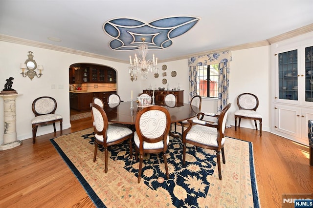 dining room featuring arched walkways, light wood-type flooring, baseboards, a chandelier, and ornamental molding
