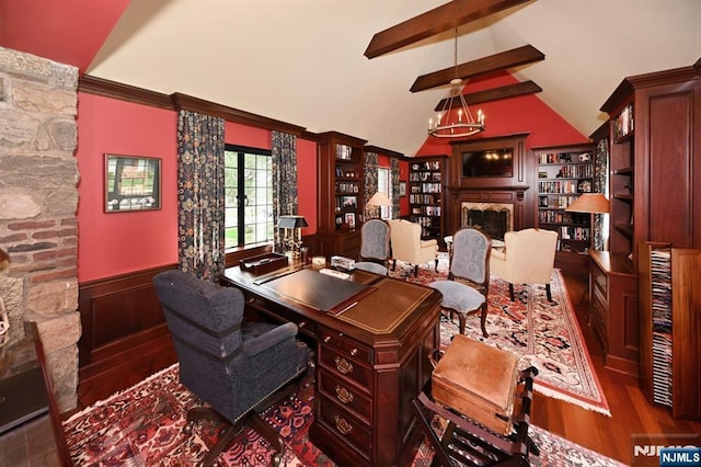 office space with an inviting chandelier, a fireplace, a wainscoted wall, vaulted ceiling with beams, and wood finished floors