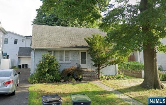 view of front of home featuring brick siding, roof with shingles, and a front yard
