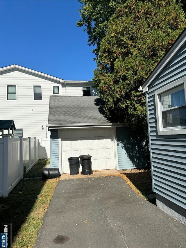 exterior space with a garage, fence, aphalt driveway, a shingled roof, and an outbuilding