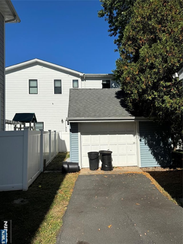 view of home's exterior with fence, an outdoor structure, driveway, a garage, and a shingled roof