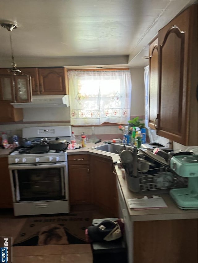 kitchen with brown cabinetry, light countertops, under cabinet range hood, and range with gas cooktop