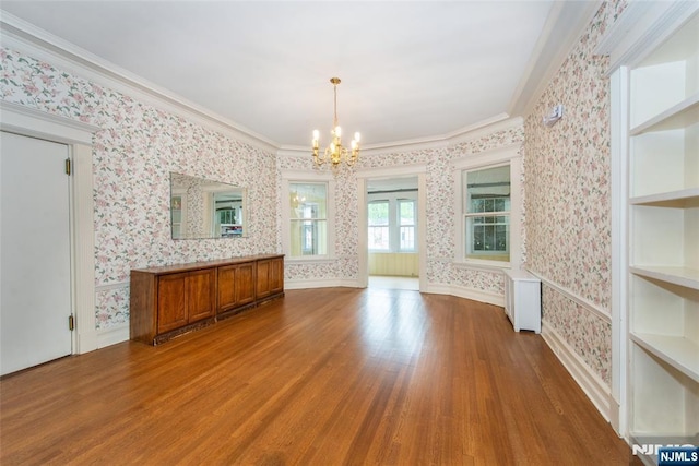 unfurnished dining area featuring radiator, wood finished floors, crown molding, an inviting chandelier, and wallpapered walls