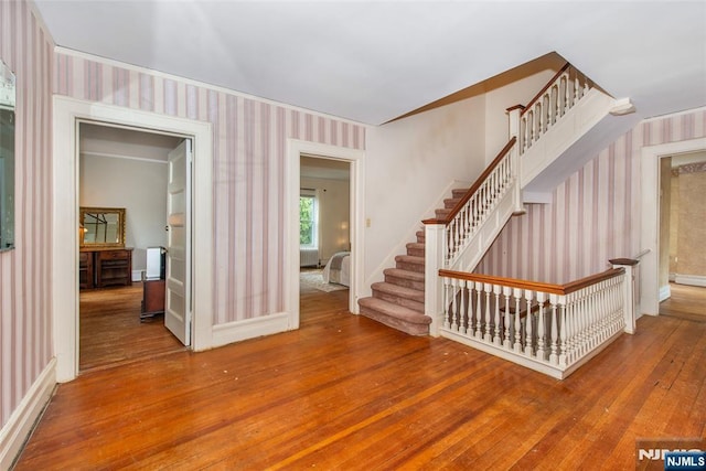 unfurnished living room featuring wallpapered walls, stairway, baseboards, and hardwood / wood-style flooring