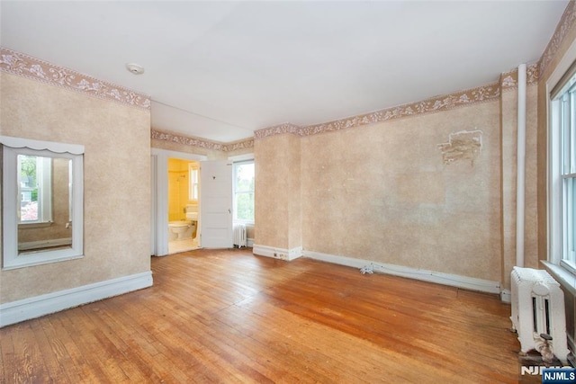 unfurnished room with baseboards, radiator, a healthy amount of sunlight, and light wood-type flooring