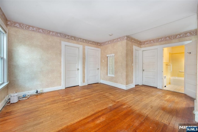 unfurnished bedroom featuring ensuite bathroom, wood-type flooring, and baseboards