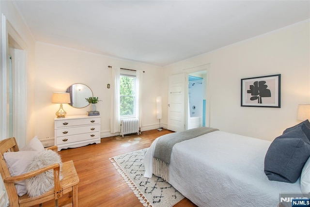 bedroom featuring ornamental molding, ensuite bath, radiator heating unit, and light wood-type flooring