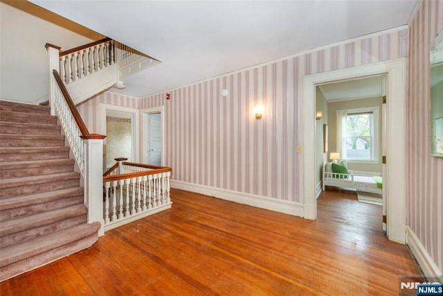 unfurnished living room with baseboards, stairs, wood-type flooring, and wallpapered walls