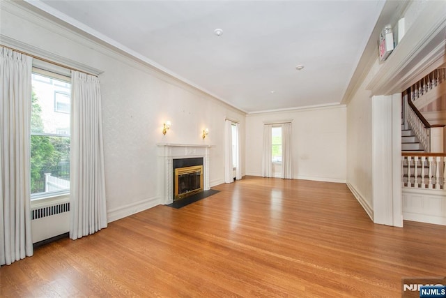unfurnished living room with stairs, radiator heating unit, light wood-type flooring, crown molding, and a fireplace with flush hearth
