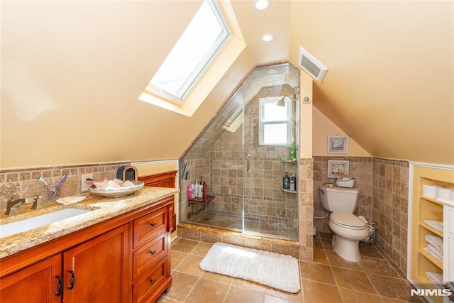 full bath with visible vents, tile walls, a stall shower, toilet, and lofted ceiling with skylight