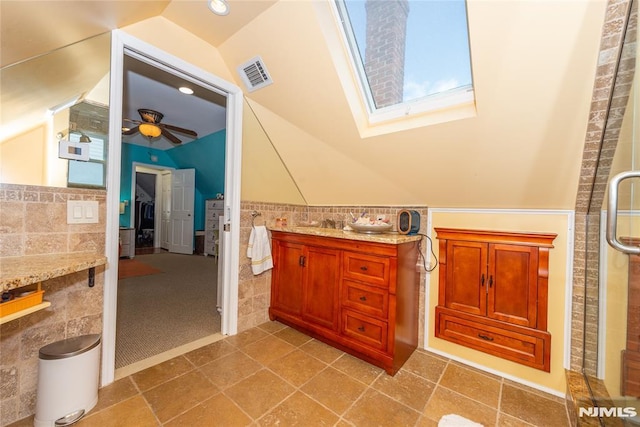 full bath featuring ceiling fan, visible vents, tile walls, wainscoting, and lofted ceiling with skylight
