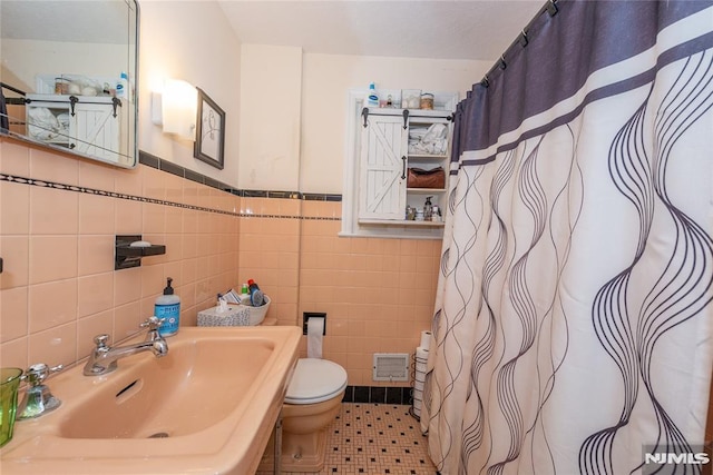 bathroom with visible vents, wainscoting, toilet, tile walls, and a sink