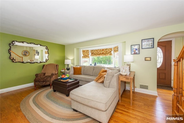 living area featuring visible vents, arched walkways, light wood-style flooring, and baseboards