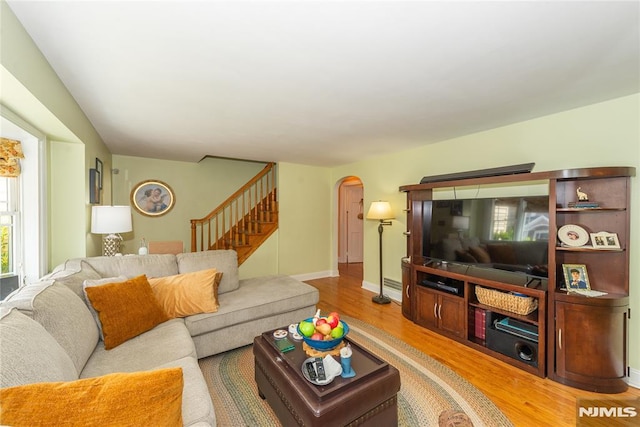 living area featuring baseboards, arched walkways, light wood-style flooring, and stairs