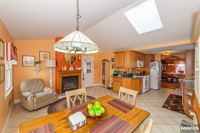 dining room with light tile patterned floors, baseboards, a glass covered fireplace, and lofted ceiling with skylight