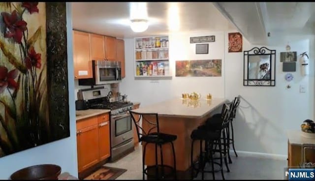 1215 Bergenline Ave, Union City, NJ 07087 - kitchen with stainless steel appliances, a kitchen bar, a peninsula, light countertops, and baseboards