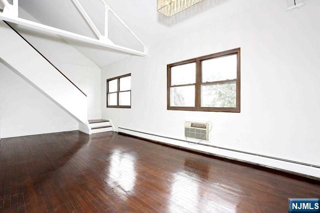57 Brookway Ave Unit 2C, Englewood, NJ 07631 - unfurnished living room featuring wood finished floors, high vaulted ceiling, stairway, a wall mounted AC, and a baseboard radiator