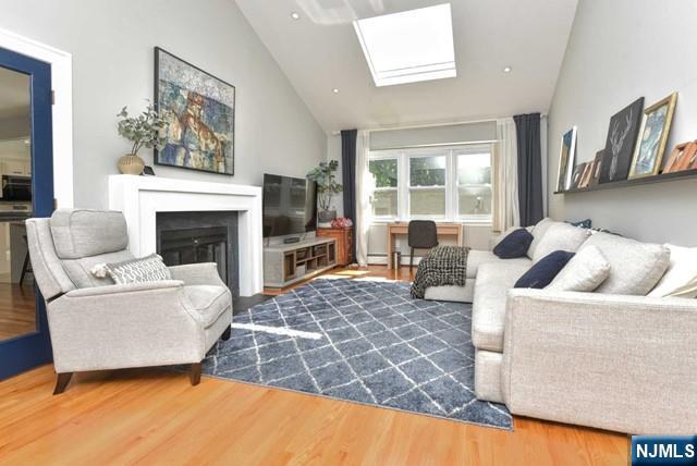 living room featuring wood finished floors, a fireplace, high vaulted ceiling, a baseboard radiator, and a skylight