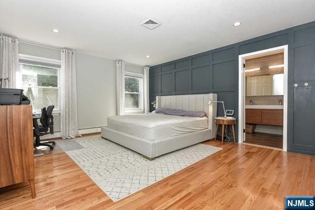 bedroom featuring light wood-type flooring, visible vents, multiple windows, and a decorative wall