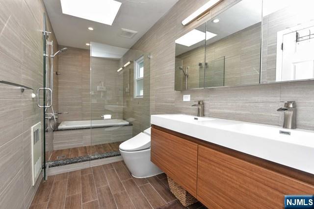 bathroom with double vanity, tile walls, a stall shower, a sink, and toilet