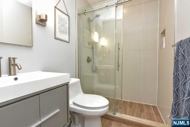 full bath featuring vanity, a stall shower, toilet, and wood finished floors