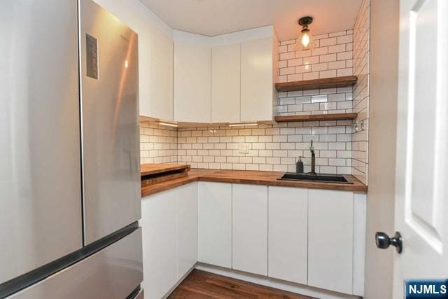 kitchen featuring freestanding refrigerator, backsplash, wood counters, and a sink