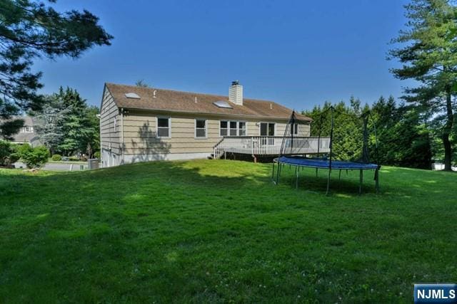 back of house with a lawn, a trampoline, a wooden deck, and a chimney