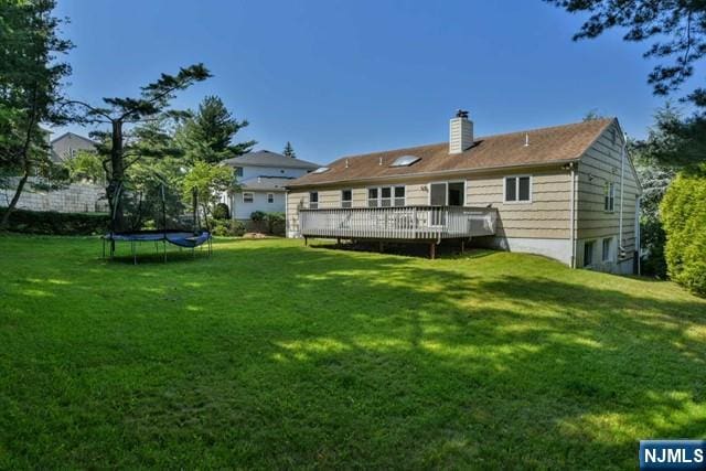 back of property featuring a lawn, a wooden deck, a trampoline, and a chimney