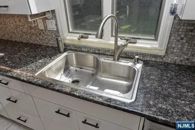 interior details with white cabinets, decorative backsplash, a sink, and dark stone countertops