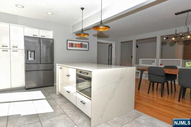 kitchen with hanging light fixtures, modern cabinets, wall oven, white cabinets, and stainless steel fridge