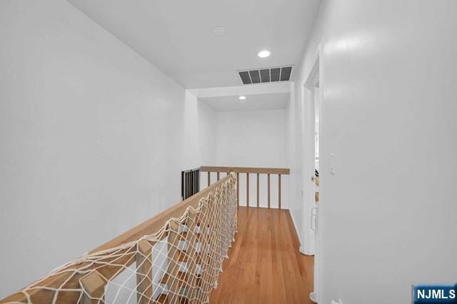 hallway with an upstairs landing, visible vents, wood finished floors, and recessed lighting