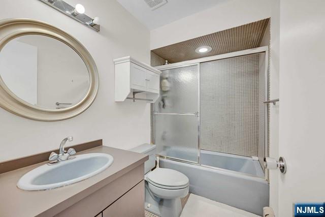 full bath with toilet, visible vents, vanity, and combined bath / shower with glass door