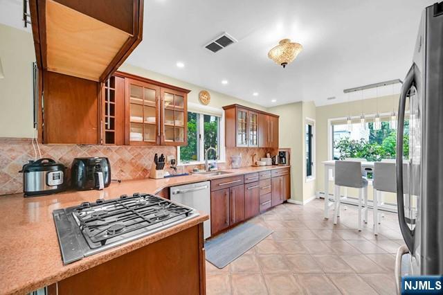 kitchen featuring a sink, brown cabinetry, visible vents, plenty of natural light, and appliances with stainless steel finishes