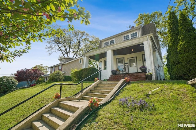 view of front facade with a front yard, stucco siding, a chimney, stairs, and a porch