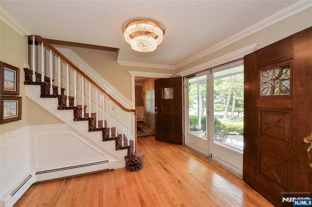 foyer featuring crown molding, stairs, a chandelier, light wood finished floors, and a baseboard heating unit