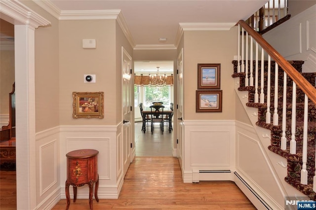 stairway with a chandelier, wood finished floors, a decorative wall, wainscoting, and ornamental molding