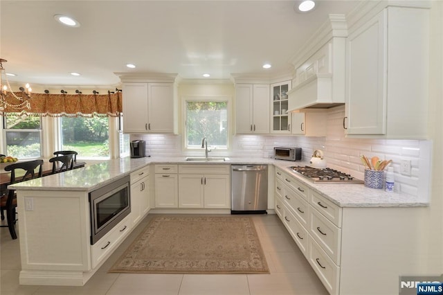 kitchen featuring appliances with stainless steel finishes, a sink, a peninsula, white cabinets, and ornamental molding