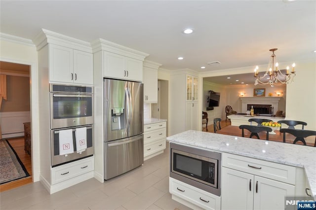 kitchen with stainless steel appliances, a baseboard heating unit, white cabinetry, light stone counters, and crown molding