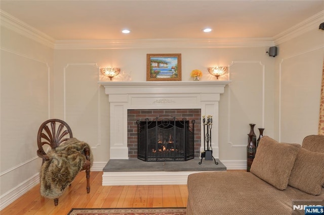 living room with a brick fireplace, ornamental molding, and hardwood / wood-style floors