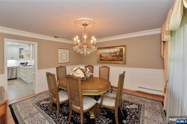 dining room with baseboard heating, a chandelier, ornamental molding, and wainscoting