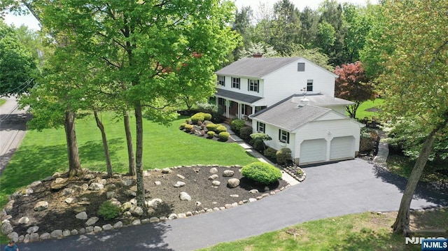 traditional home featuring driveway, a front lawn, a garage, and a chimney