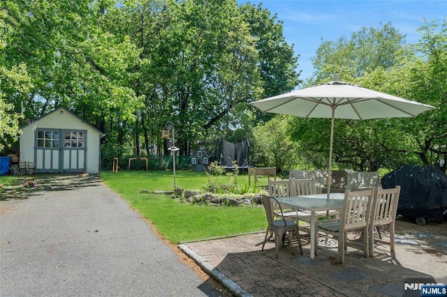 view of patio featuring a trampoline, outdoor dining area, an outdoor structure, grilling area, and a shed